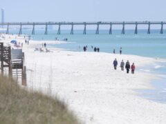 People walk along the shoreline in Navarre Beach, Florida (Nick Tomecek/Northwest Florida Daily News via AP)
