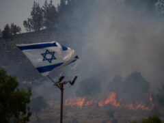 An Israeli flag flutters next to a fire burning in an area near the border with Lebanon, northern Israel (Leo Correa/AP)