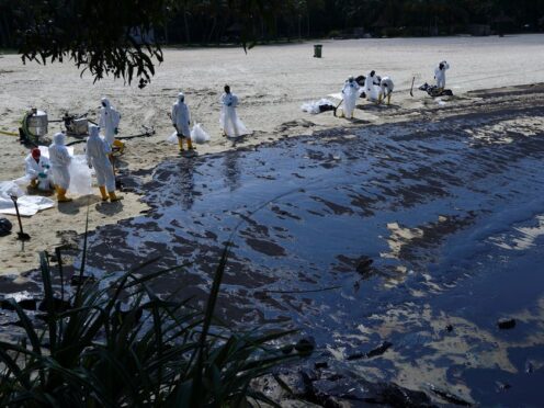 Workers clean an oil spill along Sentosa’s Tanjong Beach area in Singapore (Suhaimi Abdullah/AP)