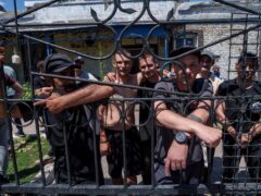 Prisoners stand behind the fence in the barracks’ yard in a prison (Evgeniy Maloletka/AP)