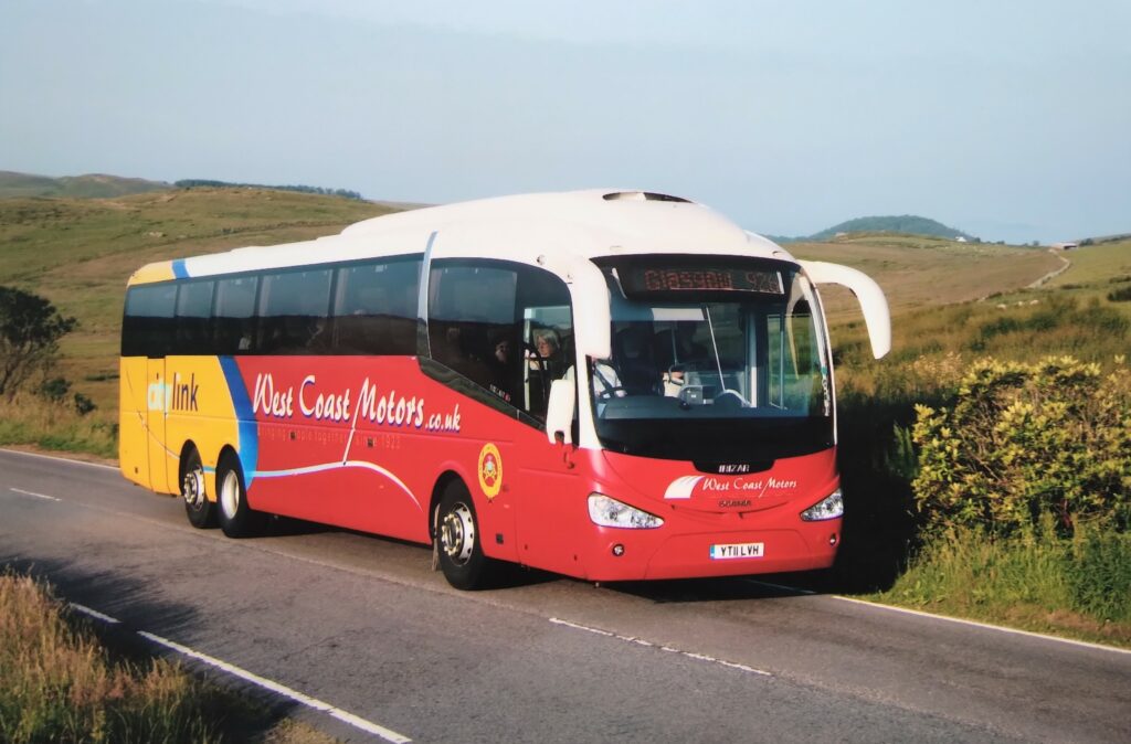 What modern age locals are familiar with: a further change of coach supplier came in 2011 when five of these striking Scania coaches came to the Glasgow service. This one is on the A83 north of Clachan and, in this early morning view, Gigha is just visible.