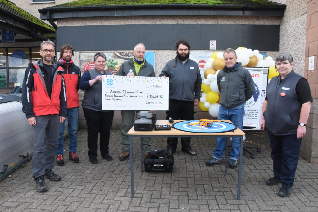 Members of the Arran Mountain Rescue Team receive their cheque from Brodick Co-op manager Liz Mclean with their newly purchased drone on display