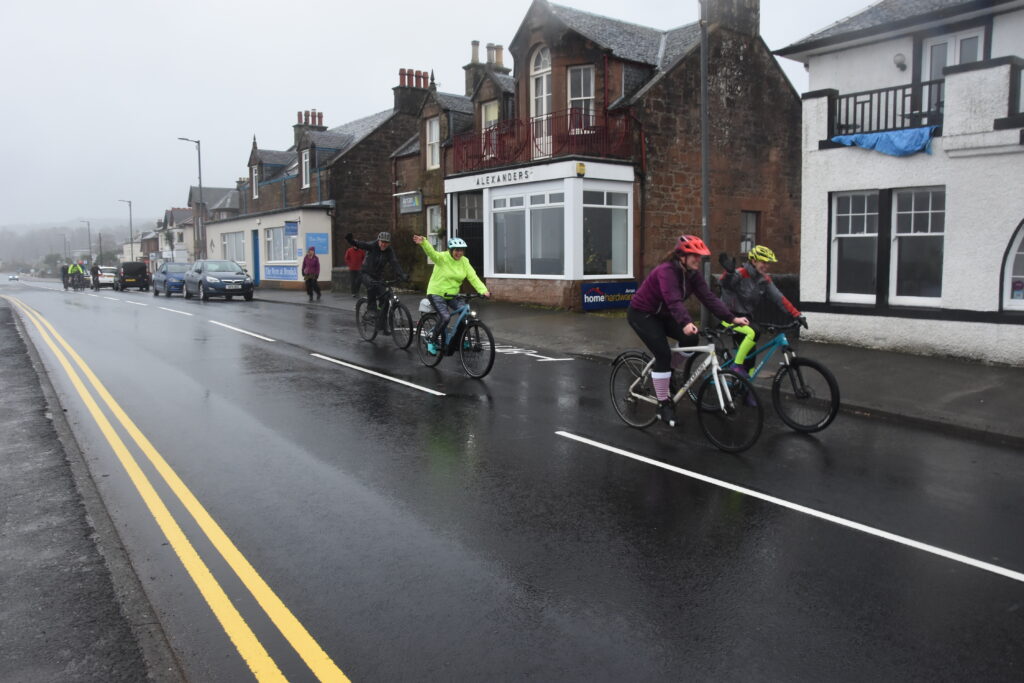 The cyclists wave to wellwishers as they pass.
