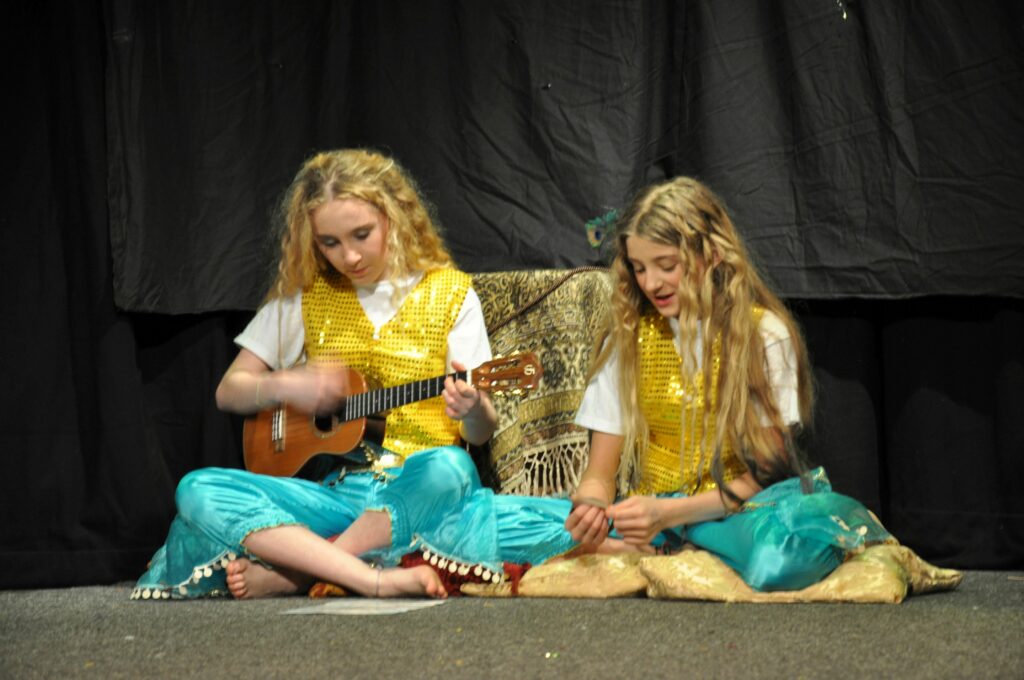 Day-Glo, played by Laura Coyle, and Mee-Too, played by Nina Szwalec, perform on the ukulele and sing.