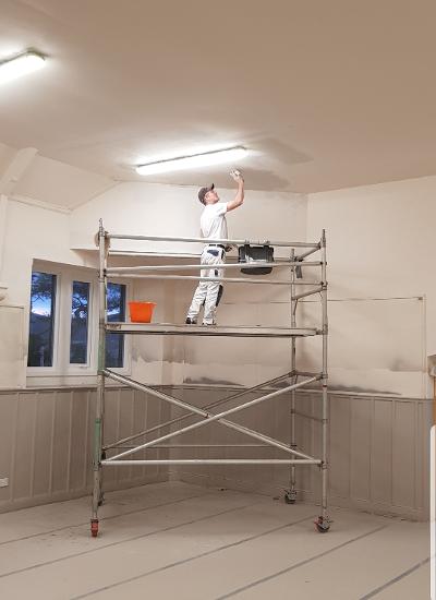 A workmen hand paints the ceiling of the hall.