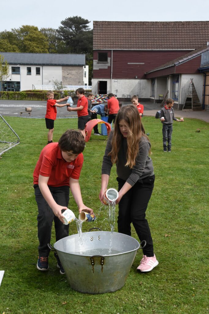 Pupils use innovative methods to transport water using broken cups, plastic bags and different sized containers.
