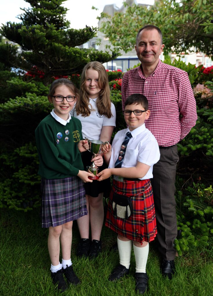 Esme McLeod  back left hands over the Chrissie McLeod Memorial Trophy to Duncan MacNeil Oban and district Provincial Mod with joint winners Lucy Spreadbury and U'isdean Craig awarded over all the sections to the most exceptional competitor  across all conversational section . A brand new trophy presented by the mcleod family