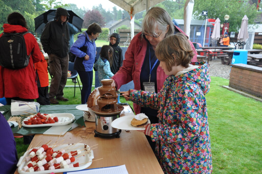 A youngster dips her strawberry and marshmallow kebab in the chocolate fountain.