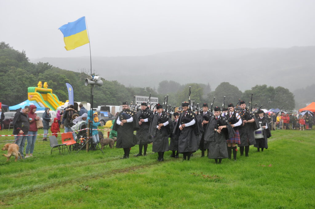 The Isle of Arran Music Schools' Pipe Band play in the wind and rain as the Ukraine flag flies over the showfield.