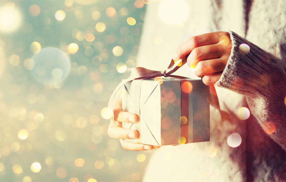 Glitter background, woman in white jumper holds white and gold wrapped present