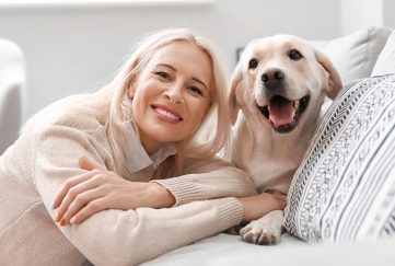 Mature woman looking happy with her pet Labrador, both at home on the sofa