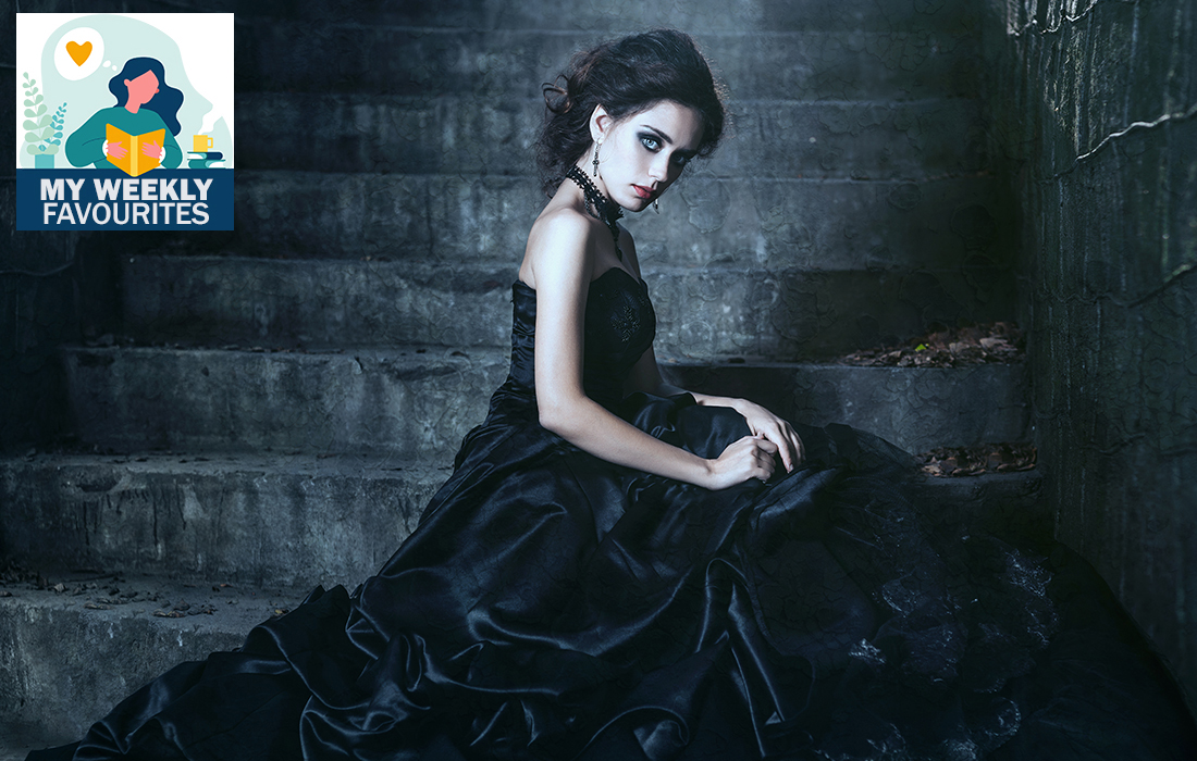 Goth girl in long black silky dress sits on dark flight of stepssteps