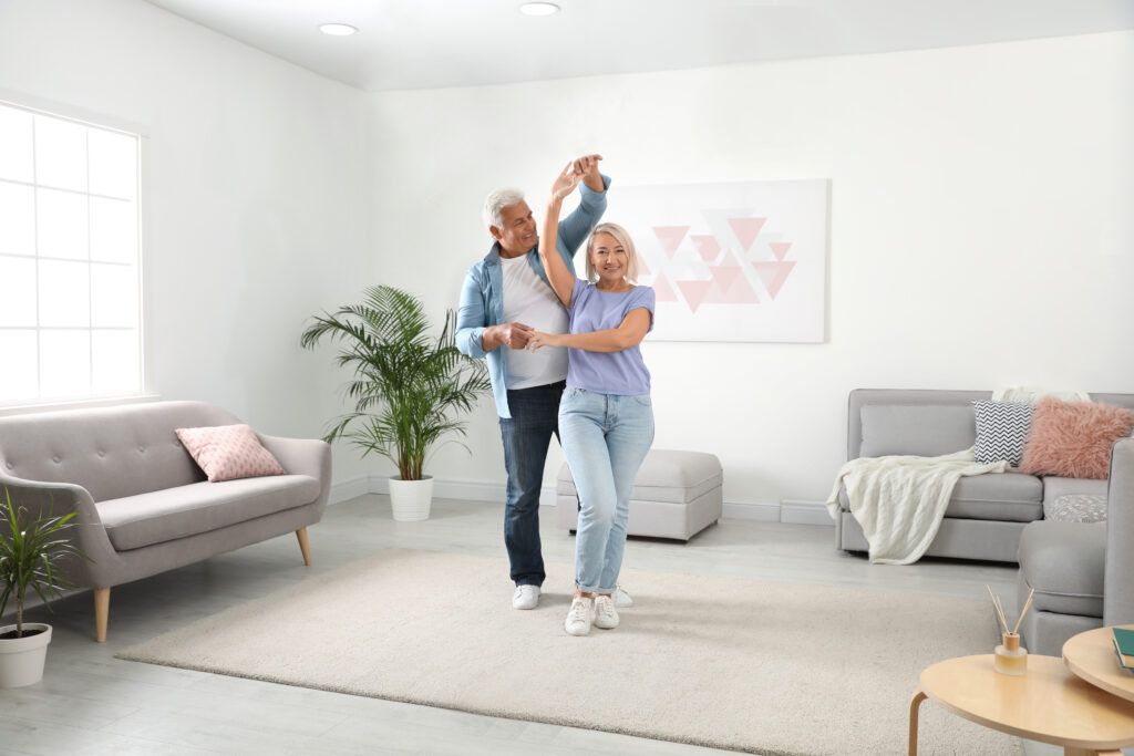 Happy mature couple dancing together in living room; 