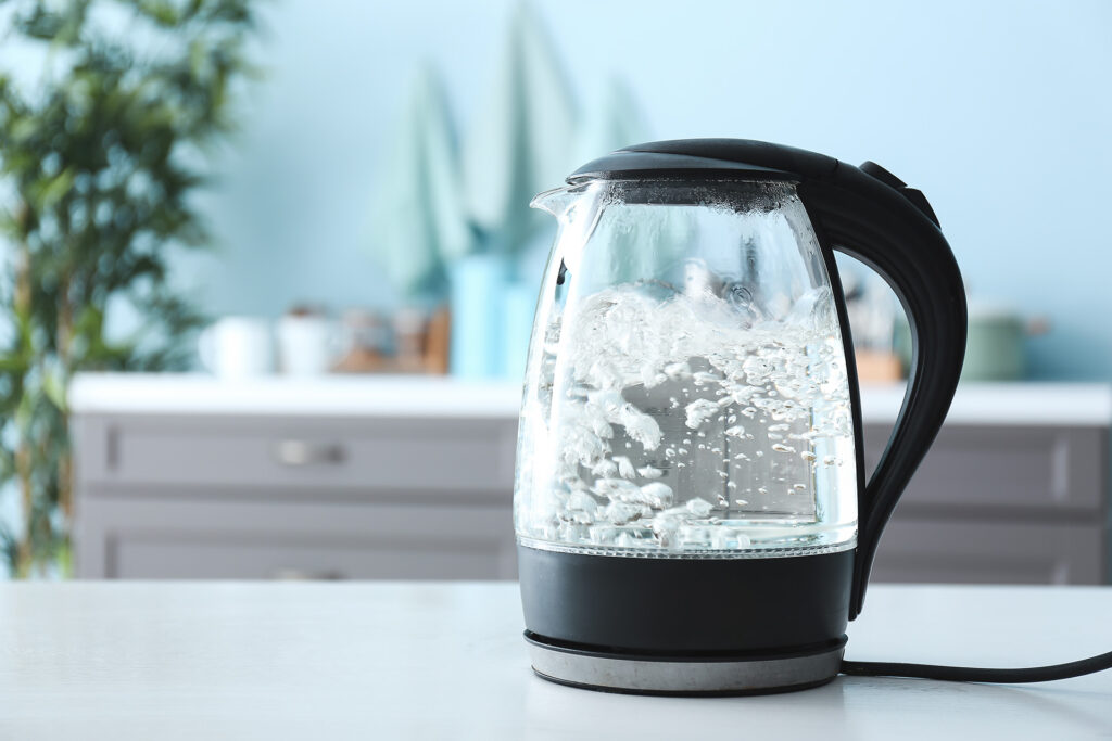 Transparent electric kettle with boiling water on table in kitchen;