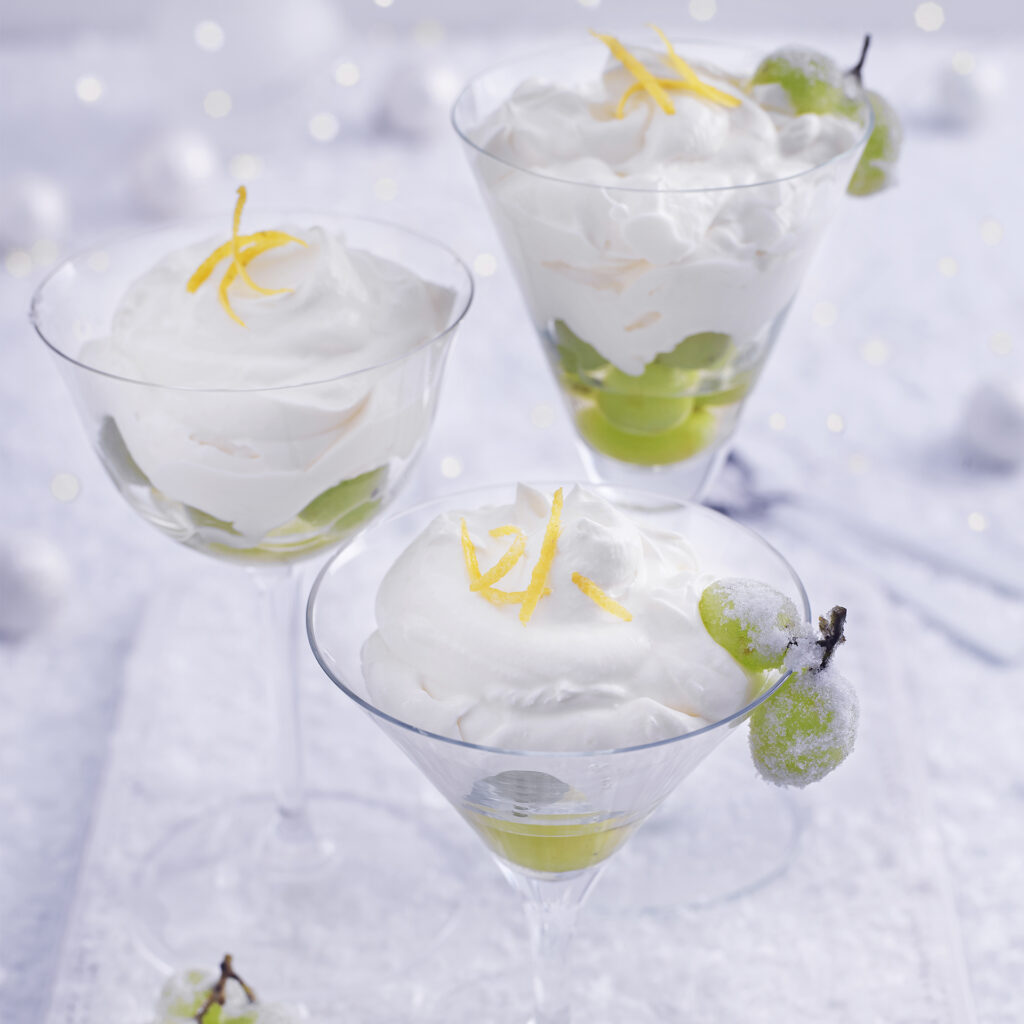 3 glass dishes of snowy white syllabub topped with lemon zest and frosted green grapes