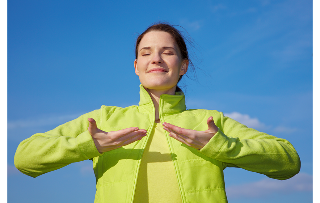 Woman in lime green jacket doing breathing exercises against a blue sky