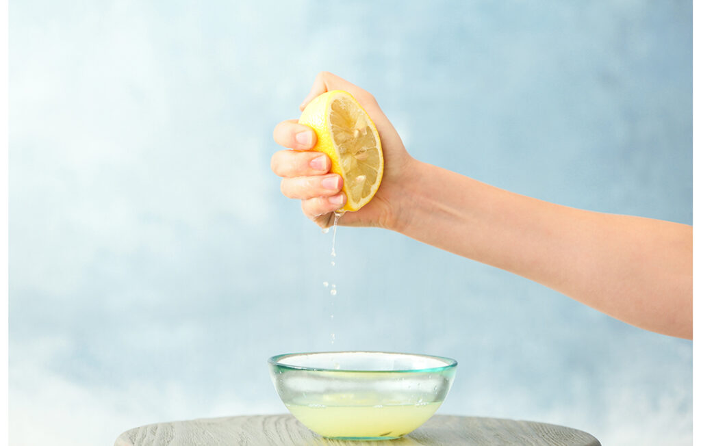 Young woman squeezing lemon juice into bowl on colour background; 