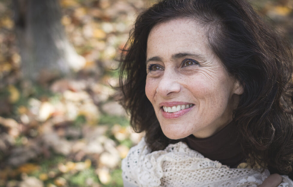 Joyful mature woman portrait in the park at fall season. Smiling middle aged lady with positive, optimistic look. Dreamer expression.