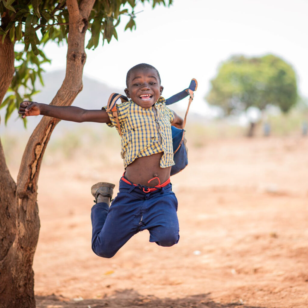 10 year old Zambian boy leaps joyfully in the air beside a tree