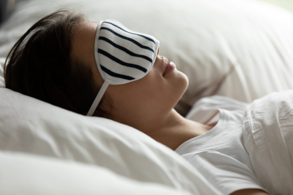 Calm young woman wearing eye sleeping mask relax take nap in comfortable white bed in hotel, peaceful millennial girl sleep rest in cozy bedroom furniture at home, relaxation, 