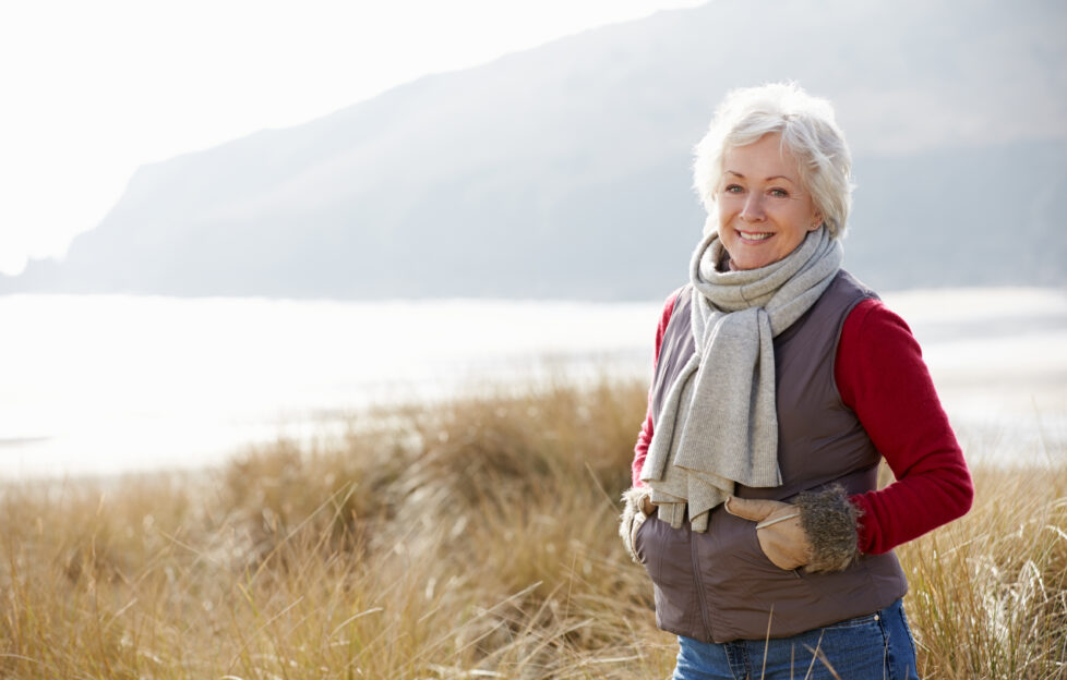 Senior Woman Walking Through Sand Dunes On Winter Beach;