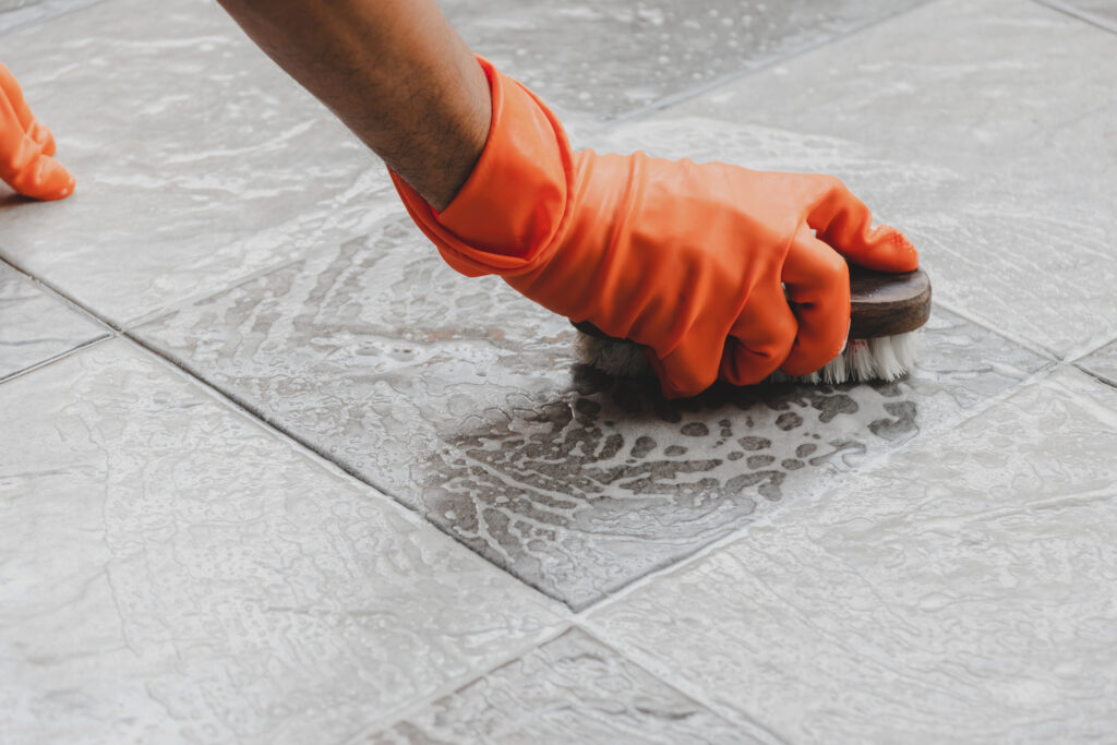 Hand of man wearing orange rubber gloves is used to convert scrub cleaning on the tile floor.; 