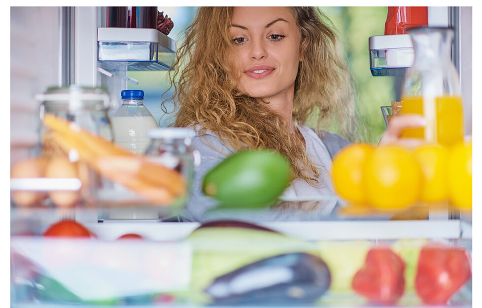 Woman standing in front of fridge full of groceries and looking something to eat. Picture taken from the inside of fridge