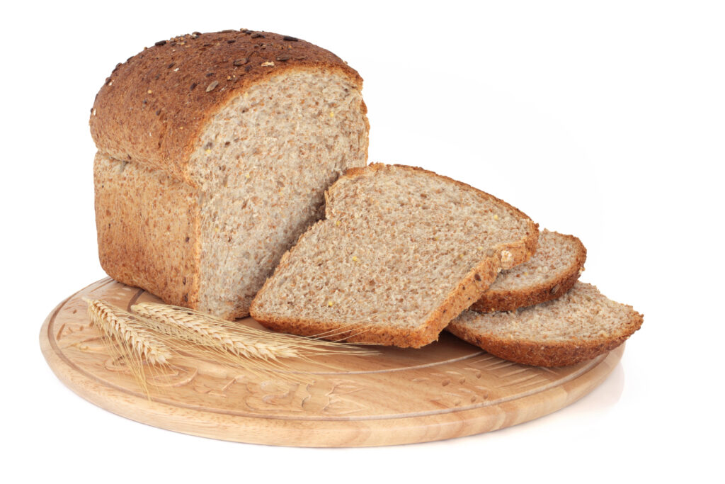 Whole grain loaf on a rustic carved wooden bread board with wheat ears isolated over white background.; 