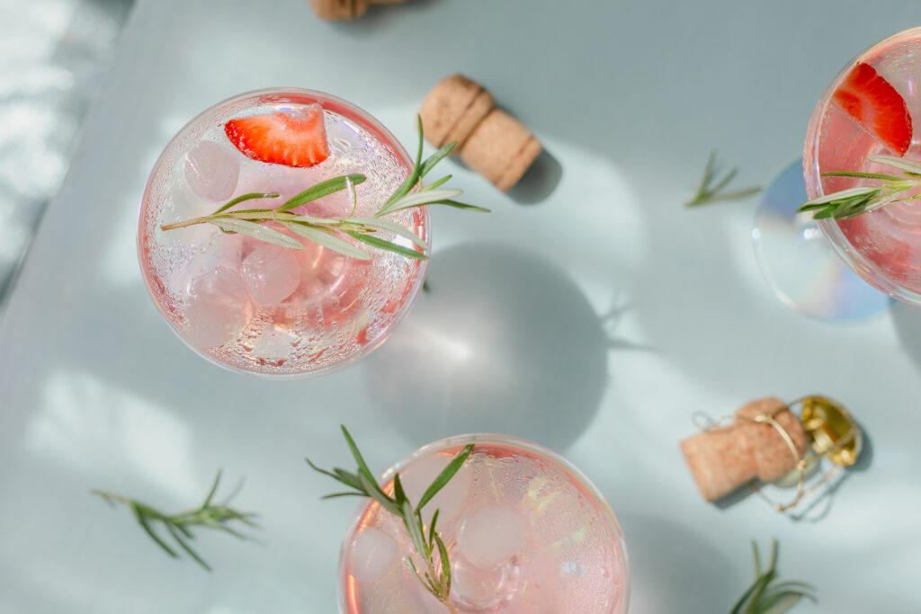 Summer drink with white sparkling wine. Homemade refreshing fruit cocktail or punch with champagne, strawberries, ice cubes and rosemary on light blue background