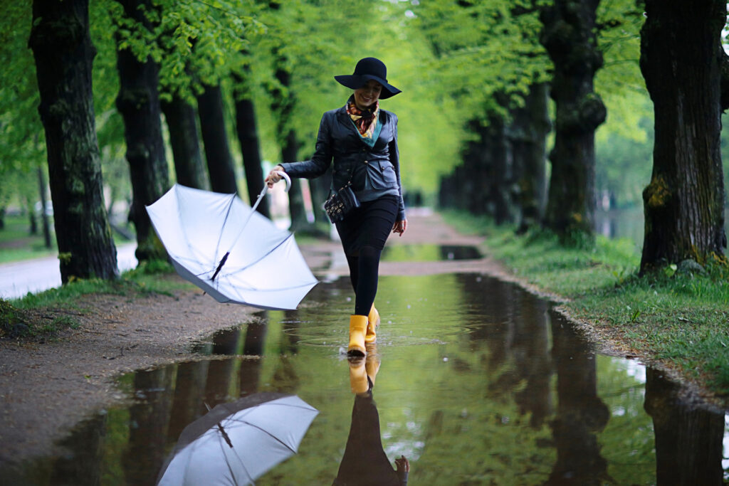 Woman walking in the rain in a park. Wearing yellow boots and holding an umbrella. Enjoying spring wellness.