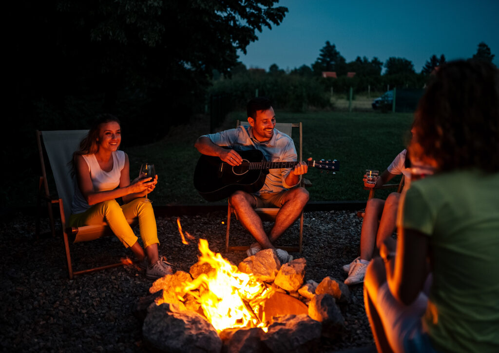 Group of friends enjoying music around the firepit at night.; Shutterstock ID 1143836348; purchase_order: 06.04.2022; job: summer garden trends MW online
