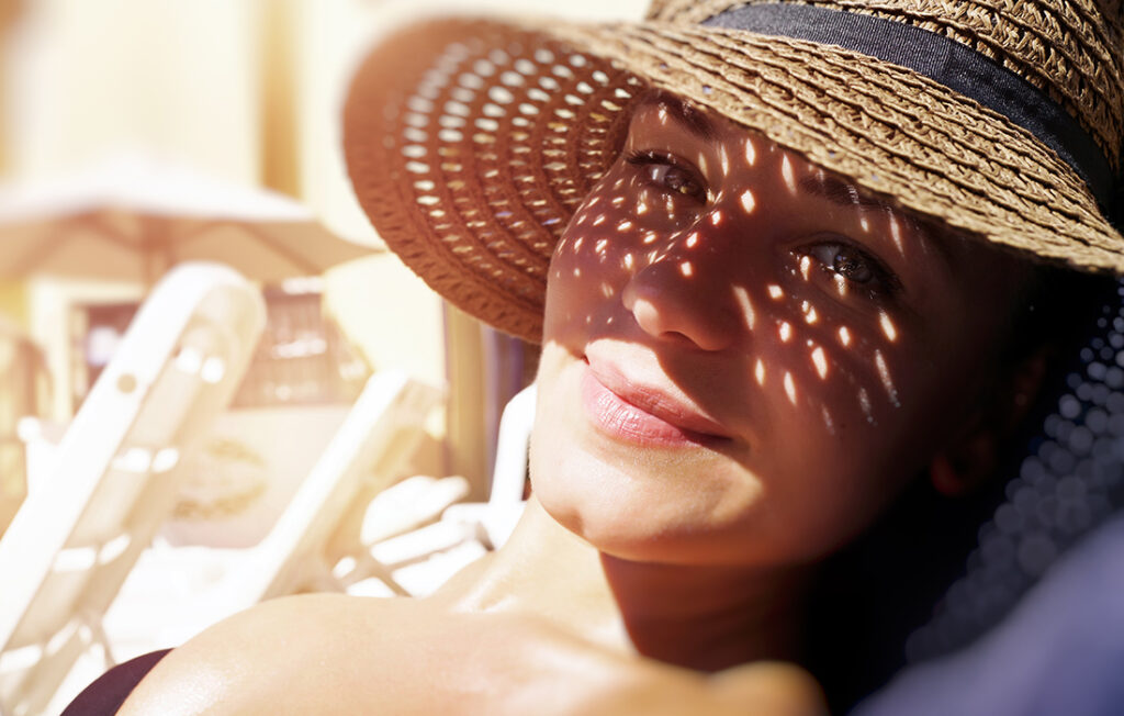 Pretty woman on the beach, closeup portrait of a nice female hides her face from the sun under a straw hat, skin protection, happy healthy summer vacation 