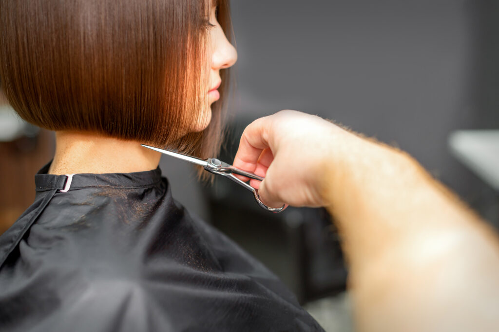 Woman having a new haircut. Male hairstylist cutting brown hair with scissors in a hair salon; 
