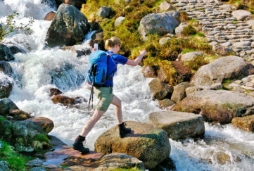 Female hiker crossing a small mountain stream on stepping stones;