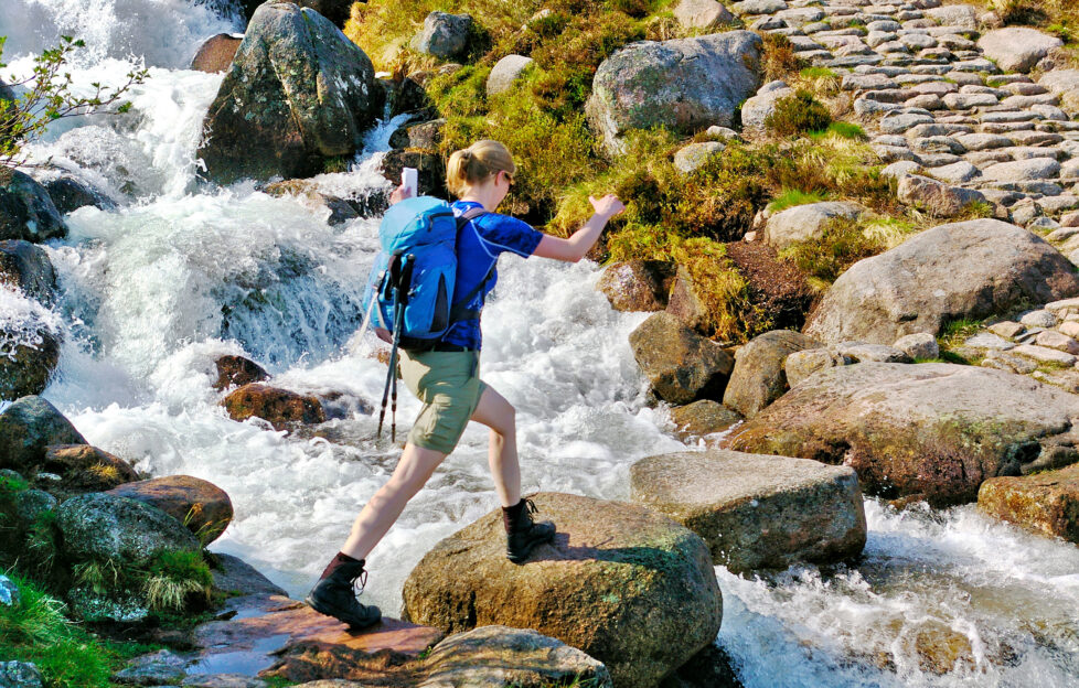 Female hiker crossing a small mountain stream on stepping stones;