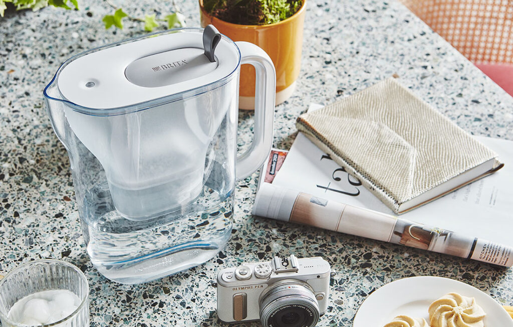 BRITA water jug siting beside newspaper and camera on granite tabletop.