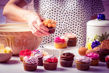 Woman in polka dot top arranging colourful iced cupcakes