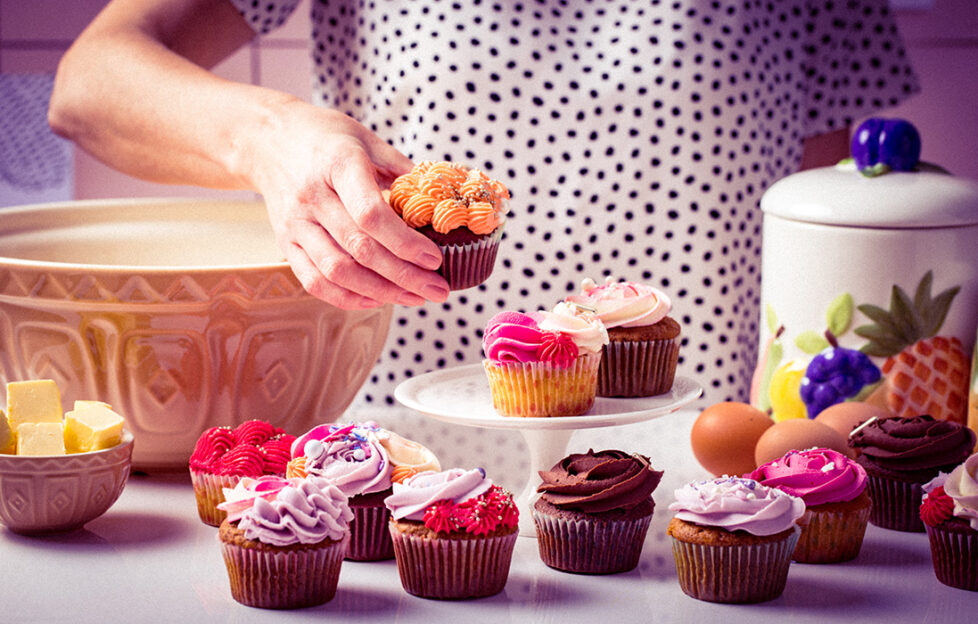 Woman in polka dot top arranging colourful iced cupcakes