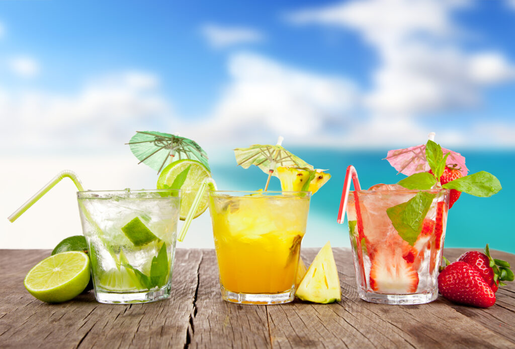 Summer cocktails with pieces of fruit on wooden table. Blur beach on background; 