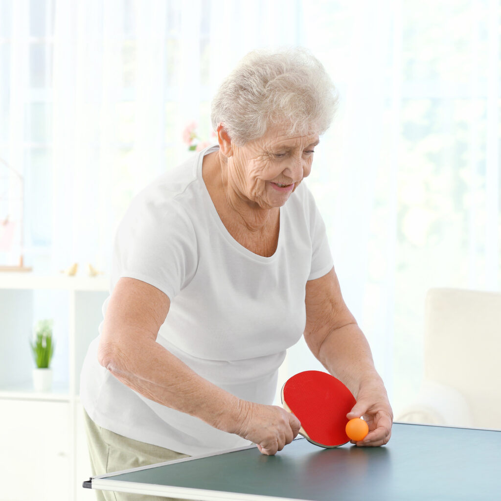 Senior woman playing table tennis indoors; 