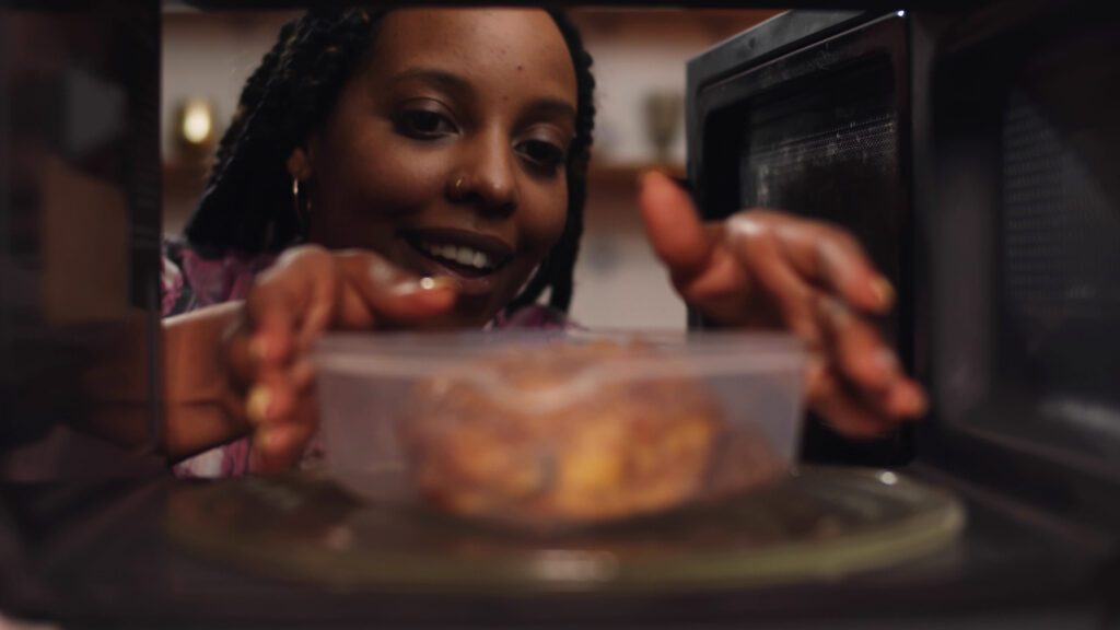 Afro-american woman using the microwave oven to heating food. View from inside microwave of african female heating up plastic container with buckwheat and chicken; 