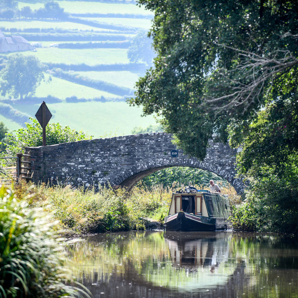 Barge approaching arched stone bridge on rural canal in Brecon, Wales
