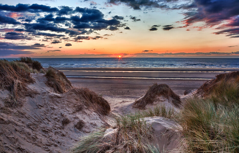 Sun setting over the beach at Formby in England through sand dunes