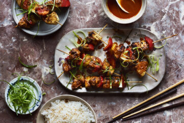 satay chicken skewers on a plate with chopsticks and garnish