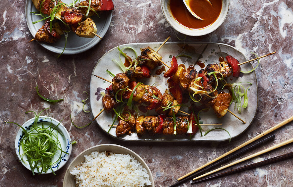 satay chicken skewers on a plate with chopsticks and garnish