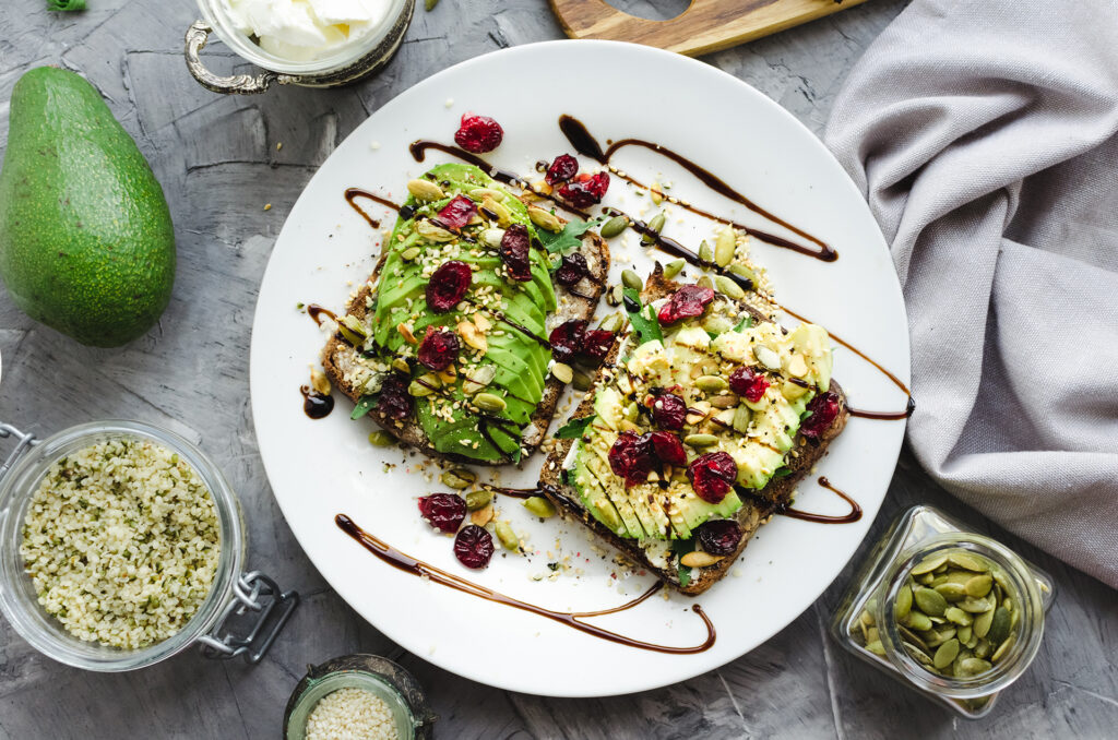 Healthy avocado toasts for breakfast or lunch with rye bread, cream cheese, arugula, sliced avocado, dried cranberry, pumpkin, hemp and sesame seeds. Vegetarian sandwiches. Clean eatiing