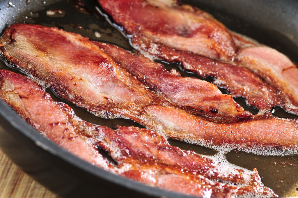 Bacon strips sizzling on a frying pan; 
