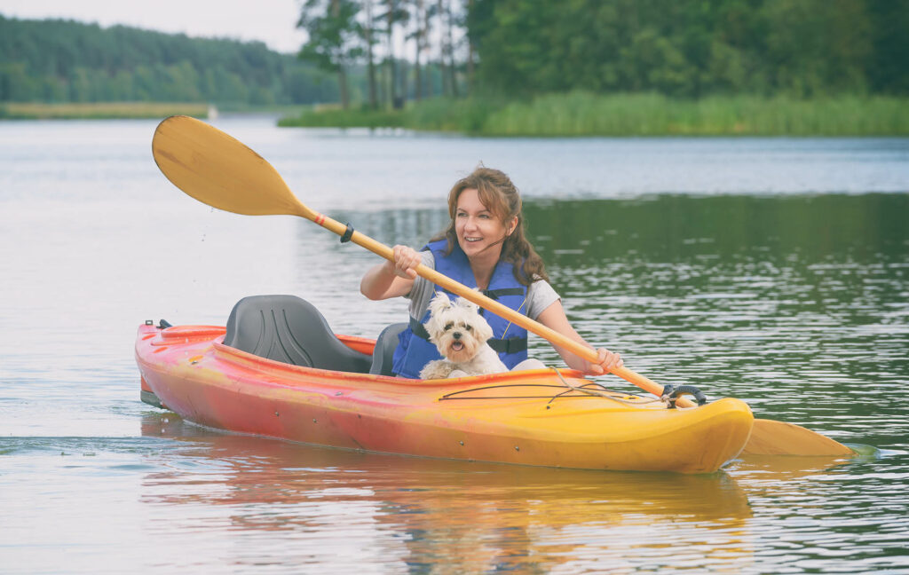 Woman in canoe on lake with small white dog