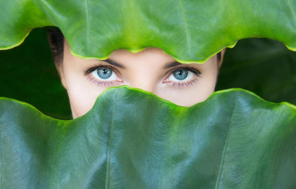 Young woman's face surrounded by tropical leaves.