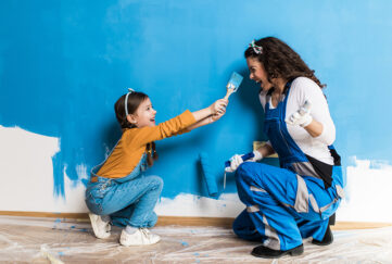 Mother and daughter dabbing paint on nose while painting wall.